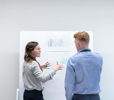 Two engineers discuss work at a whiteboard