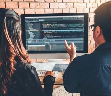 Engineers discuss a coding project while sitting at a computer